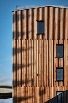 a tall wooden building with two windows on the side and a bridge in the background