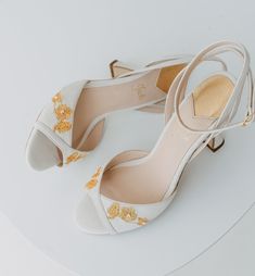 a pair of white high heel shoes with gold flowers on the toes and heels are sitting on top of a round table