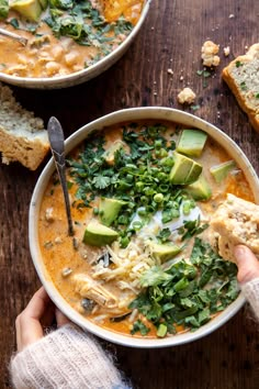 two bowls of soup with bread and avocado garnished with cilantro