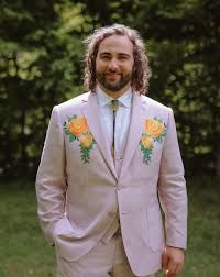 a man with long hair wearing a pink suit and orange flowers on his lapel