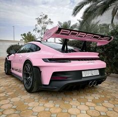 a pink porsche sports car parked in front of a palm tree with its hood up