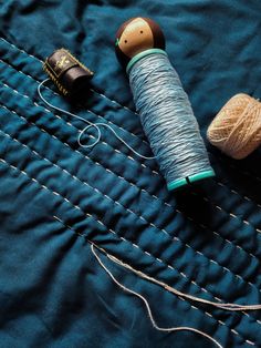 two spools of thread sitting on top of a blue piece of cloth next to some wooden pegs