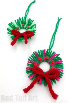 two small christmas wreaths with red and green yarn hanging from each one's sides