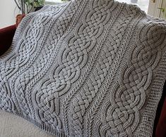 a gray knitted blanket sitting on top of a red couch next to a window