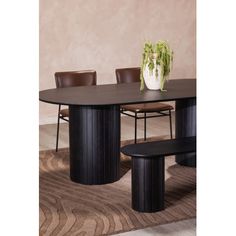 a dining table with chairs and a vase on the top, in front of a beige wall