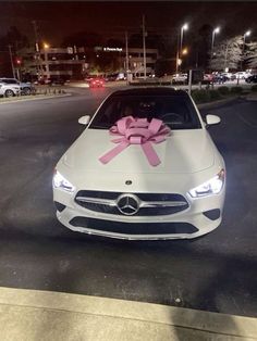 a white car with a pink bow on it's hood parked in the street