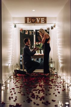 a man kneeling down next to a woman in front of a window with rose petals on the floor