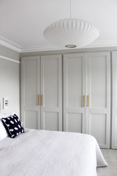 a white bed sitting in a bedroom next to closets and a light fixture above it