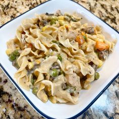 a white plate topped with pasta covered in meat and vegtables on top of a marble counter