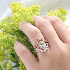 a woman's hand with a ring on top of her finger and flowers in the background