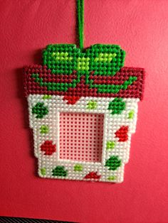 a cross stitch ornament hanging on a red wall with a green plant in it