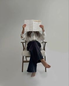 a woman sitting in a chair holding up a book to her face with both hands