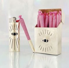 an open box with pink flowers in it next to a silver lighter and eye - shaped object