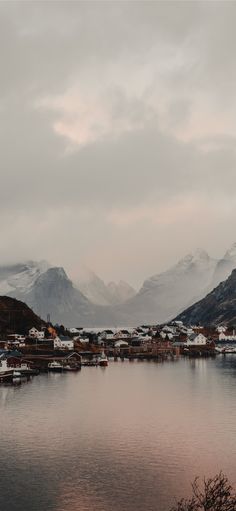 the mountains are covered in snow as boats sit on the water and houses line the shore