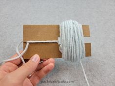 someone is holding a twine of string in their hand while they are making something out of cardboard