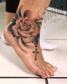 a woman's foot with a rose and cross tattoo on the top of it