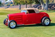 an old red car parked on top of a lush green field