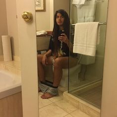 a woman is sitting on the toilet taking a selfie with her cell phone in a bathroom