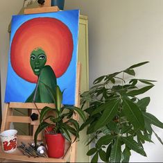 a painting on an easel next to a potted plant