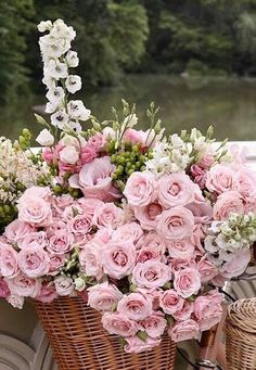 a basket filled with pink and white flowers on top of a table next to a bicycle