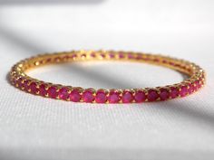 Designed in the USA, handcrafted with love by our female artisans in India this beautiful Bangle Set comes in a gold plated finish with stunning Red Ruby lab grown stones to make this exquisite Bangle Set really special - light in weight & can be paired with almost any outfit. Perfect accessory for every jewelry box!  - Handcrafted  - Metal: Metal Alloy, Gold Plated  - Stone: American Diamond (Lab Grown), Ruby CZ Stones (Lab Grown)  - Size: Size 2.8 (2.5" interior width), Fits Most Wrist Sizes  - Set of 4 Bangles Please care for your product by refraining from exposing items to harsh chemicals and abrasives, water, alcohol or constant direct sunlight.  Please store items in provided padded box.  A soft cloth and gentle swipe will bring your items back to luster once removed for next time u Adjustable Gemstone Bangle For Wedding, Gold Ruby Stackable Jewelry, Gold Bangle With Prong Setting For Anniversary, Wedding Bangle With Gemstone, Gold Plated Round Bangle For Wedding, Gemstone Round Bangle For Wedding, Ruby Gemstone Bangle For Wedding, Yellow Gold Ruby Bracelets For Wedding, Yellow Gold Gemstone Bangle For Wedding