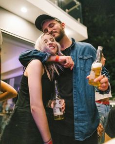 a man and woman hug each other while holding beer bottles