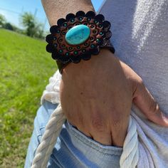 "Brown leather bracelet that has a paisley filigree. It is adorned with turquoise cabochon concho and a hand painted leather rosette. Measures 7.75\" to 8.25\" with two snaps for adjustment." Adjustable Hand Tooled Western Leather Bracelet, Western Style Turquoise Leather Bracelets, Western Style Turquoise Bracelet, Hand Tooled, Turquoise Leather Concho Bracelets, Turquoise Leather Concho Jewelry, Adjustable Turquoise Cuff Bracelet With Concho, Adjustable Hand-tooled Turquoise Cuff Bracelet, Adjustable Turquoise Leather Bracelet With Concho, Adjustable Hand Tooled Turquoise Cuff Bracelet