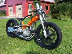 an orange motorcycle parked in front of a red barn