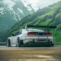 the rear end of a white sports car on a road with mountains in the background