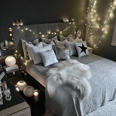 a bed with white pillows and lights on the headboard is decorated in black and silver