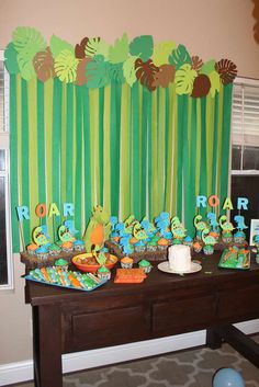 a table topped with lots of cake and cupcakes next to a wall covered in jungle animals