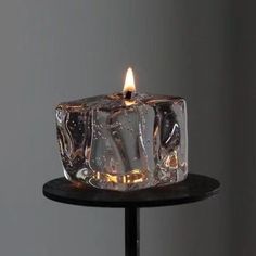 an ice cube candle is lit on a black table with a gray wall in the background