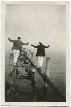 two people are standing on a dock with their arms spread out to the water and one person is holding his hands out