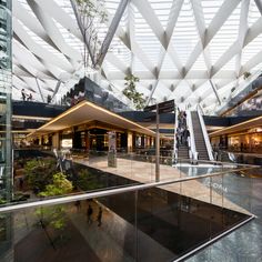 people are walking around in an indoor shopping mall with glass walls and ceiling lights above them