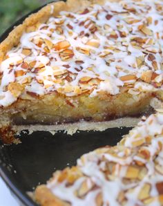 a pie with white frosting and almonds on top is sitting on a pan