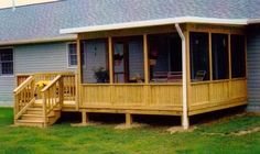 a wooden porch sitting on top of a green grass covered field next to a house