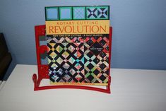 a book is sitting on top of a red rack that has a quilt in it