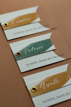 three name tags with gold, green and white ink on them are placed next to each other