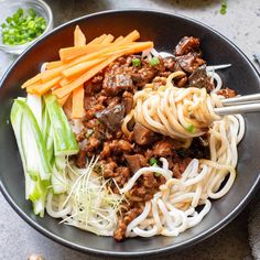 a bowl filled with noodles, meat and veggies on top of a table