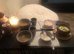 a table topped with bowls of food next to a candle and two cups filled with soup