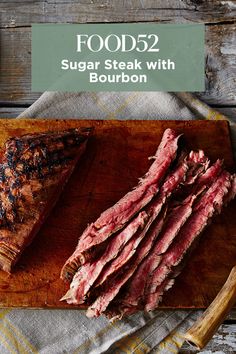 sliced steak on wooden cutting board with knife and fork next to it, text reads food52 sugar steak with bourbon