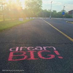 the word dream big written in chalk on an empty street with grass and trees behind it