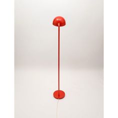 a red floor lamp sitting on top of a white table next to a light bulb