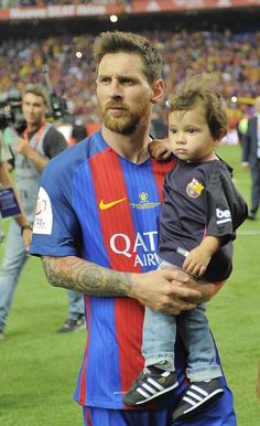 a man holding a small child in his arms on the field at a soccer game