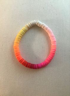 a bracelet made out of colored paper on a white tablecloth with an orange, pink, yellow and green bead