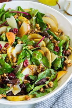 a salad with apples, pears and cranberries in a white bowl on a marble table