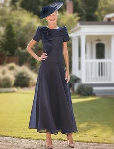 a woman standing in front of a house wearing a dress and hat