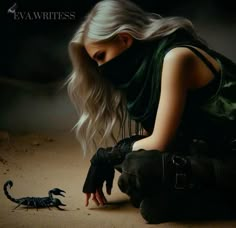 a woman kneeling down in front of a scorpion on the ground next to her hand