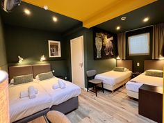 two beds in a room with green walls and wood flooring, one is white and the other is brown