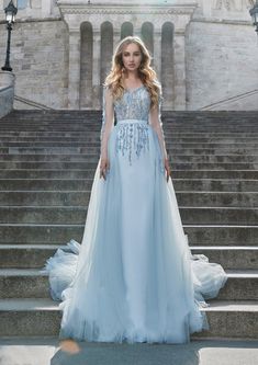 a woman in a blue dress standing on some steps with her hands behind her back